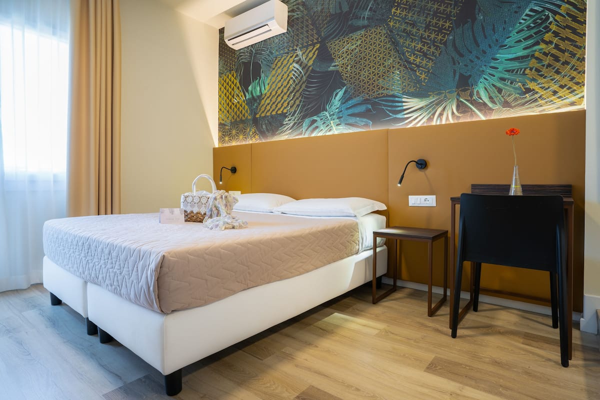 A hotel room with a bed, bedside tables, a desk, and a large abstract mural on the wall.