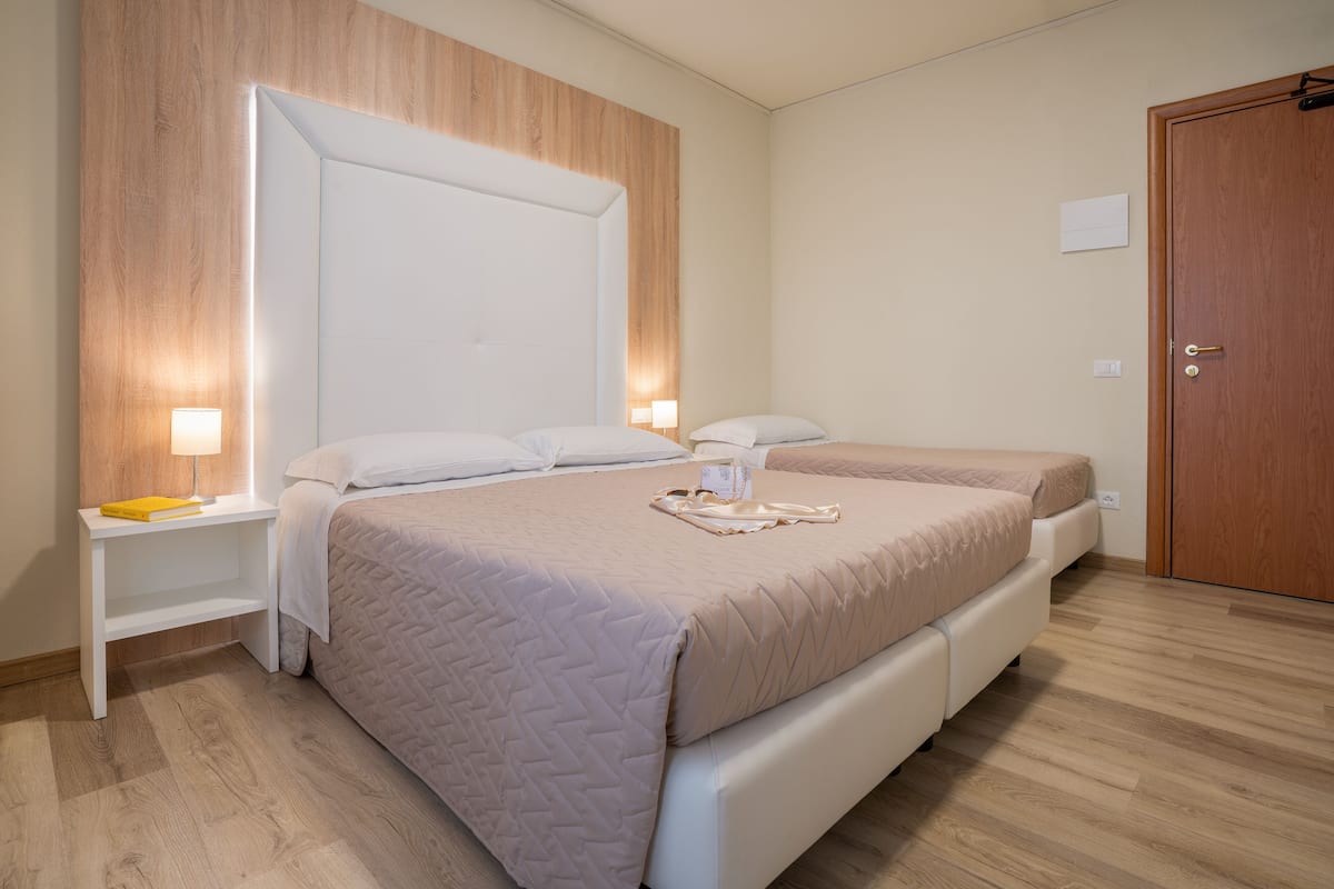 A bedroom with two beds, a wooden headboard, bedside tables with lamps, and a wooden door.