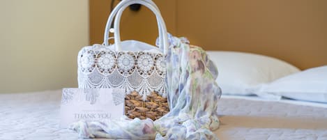 A white, intricately designed basket with a handle on a bed with a white pillow and a headboard.