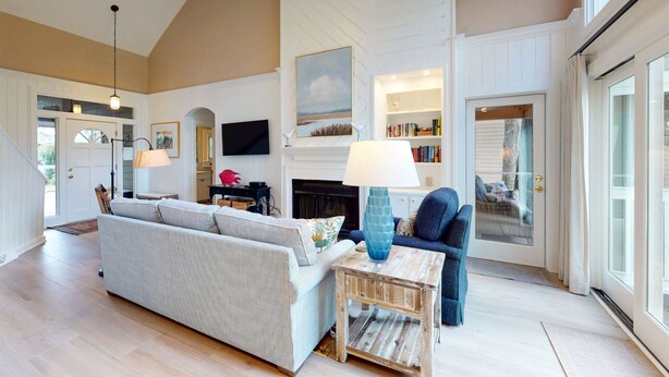 A spacious living room with a high ceiling, a fireplace, a television, and a large window.