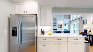 A modern kitchen with white cabinetry, a stainless steel refrigerator, and a central island with a yellow bowl.