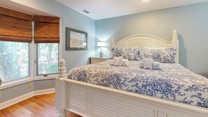 Un dormitorio con cama, una ventana con persianas, ventilador de techo y mesita de noche con lámpara.