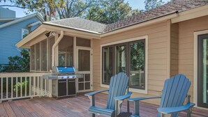 Una terraza techada al aire libre con una parrilla, dos sillas Adirondack y un banco.