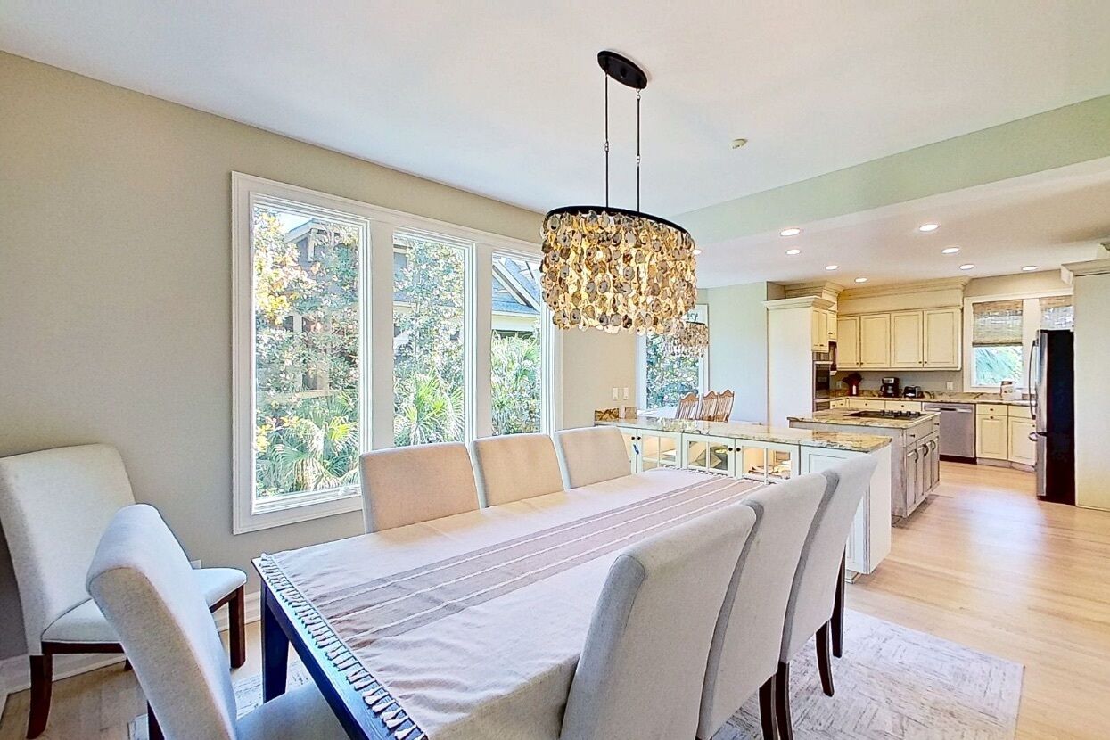A modern kitchen with a central island, large windows, and a dining area with a long table and chairs.