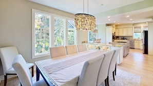 Una cocina moderna con una isla central, ventanas amplias y un comedor con una mesa larga y sillas.