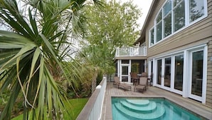 Un patio trasero con piscina, terraza de madera y zona cubierta con mobiliario exterior.