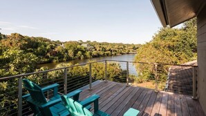 Une terrasse en bois avec des chaises vertes donnant sur une rivière, entourée d’arbres.