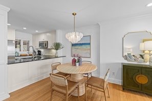 A modern kitchen with white cabinets, a black countertop, and a wooden dining table with four chairs.