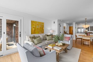 A modern living room with a sofa, coffee table, and a dining area with a chandelier.