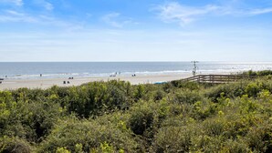 A beach with a wooden boardwalk, dense greenery, and the ocean in the background. - Kiawah Exclusives | 4303 Windswept Villa (Kiawah Island)