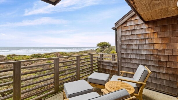 A wooden deck with a view of the ocean, a wooden fence, and a table with chairs. - Kiawah Exclusives | 4303 Windswept Villa (Kiawah Island)