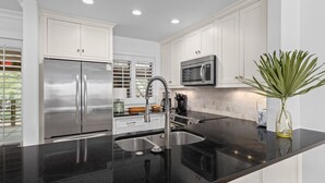 A modern kitchen with white cabinetry, stainless steel appliances, and a black granite countertop. - Kiawah Exclusives | 4303 Windswept Villa (Kiawah Island)