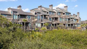 A row of houses with multiple chimneys and balconies, surrounded by dense vegetation. - Kiawah Exclusives | 4303 Windswept Villa (Kiawah Island)