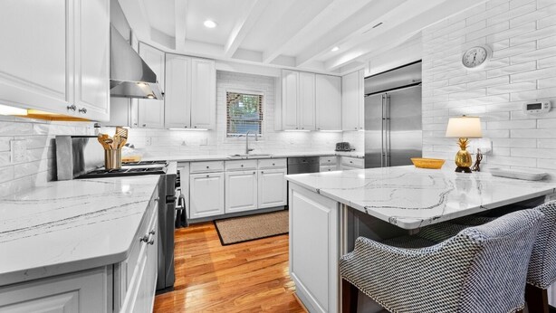 Una cocina moderna con armarios blancos, una isla de mármol, electrodomésticos de acero inoxidable y un reloj en la pared.
