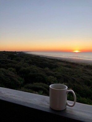 Eine Tasse auf einer Brüstung mit Blick auf einen Sonnenuntergang über einer Küstenlandschaft.