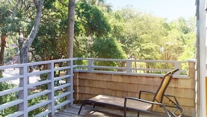 Een houten terras met een witte balustrade, een enkele metalen stoel en een houten schutting.