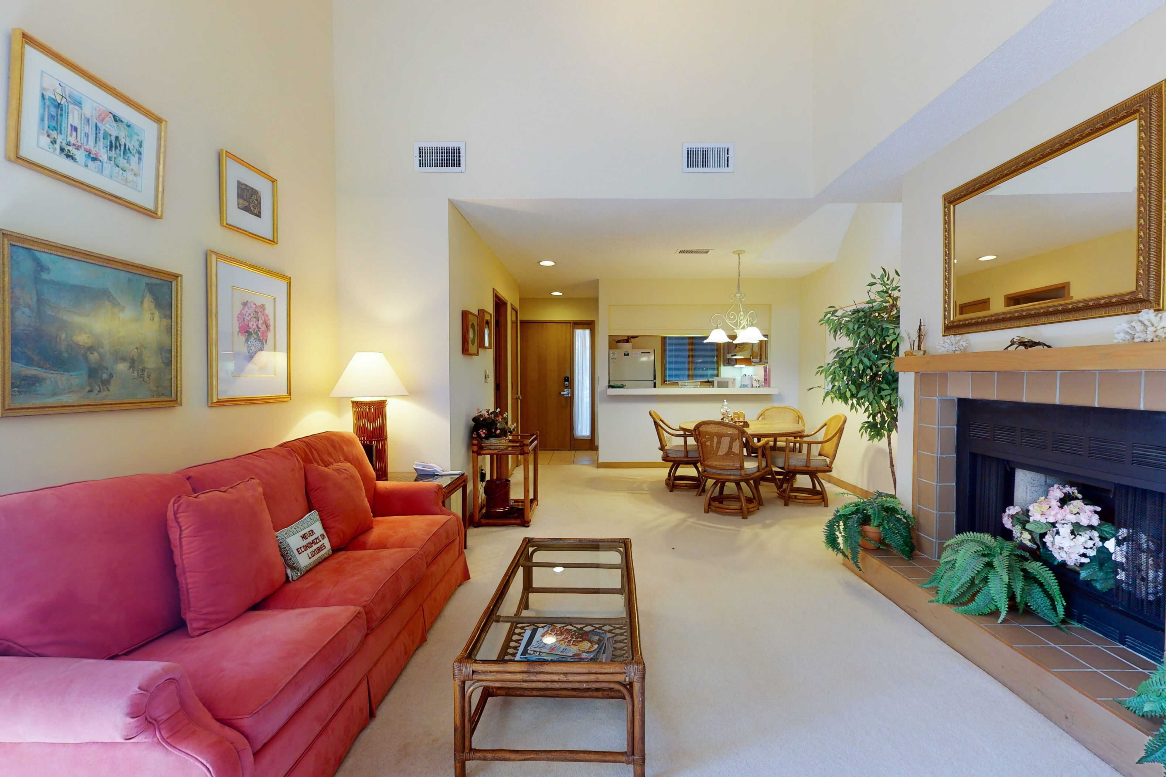 A living room with a red sofa, a glass coffee table, and a fireplace. There is a dining area with a table and chairs, and a kitchen in the background.