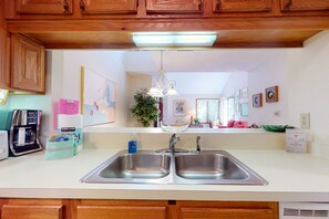 A kitchen with a double sink, wooden cabinets, a coffee maker, and a plant. - Kiawah Exclusives | 4468 Windswept Villa (Kiawah Island)