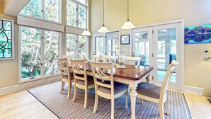 Un comedor con una mesa y sillas de madera, ventanas amplias y lámparas colgantes.