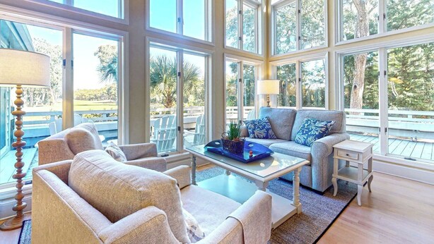 Una habitación amplia con ventanas grandes, un sofá, sillones y una mesita de centro.