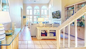 Un amplio salón con una escalera de madera, un ventanal grande y un televisor.