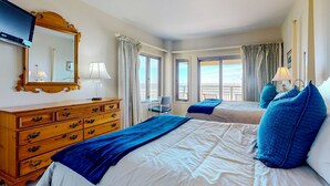 Habitación de hotel con dos camas, un aparador de madera, un televisor y un balcón con vistas.