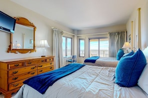 A hotel room with two beds, a wooden dresser, a TV, and a balcony with a view.
