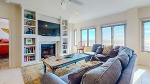 Una sala de estar con chimenea, un sofá grande y un televisor. Se observan estanterías y un ventilador de techo.