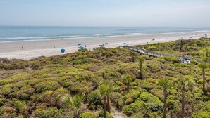 Una playa con un paseo marítimo de madera, vegetación verde exuberante y una vista despejada del océano.