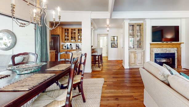 A spacious living room with a fireplace, a dining area with wooden furniture, and a kitchen with wooden cabinets. - Kiawah Exclusives | 4942 Turtle Point Villa (Kiawah Island)