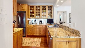 A kitchen with wooden cabinets, a stainless steel refrigerator, a granite countertop, and a built-in oven. - Kiawah Exclusives | 4942 Turtle Point Villa (Kiawah Island)