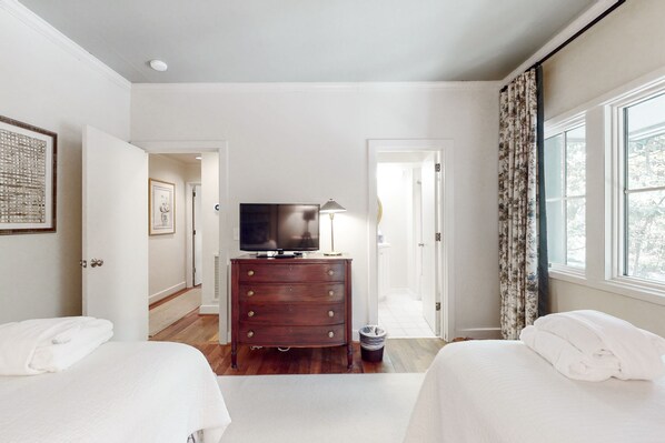 A hotel room with two beds, a dresser, a television, and a window with curtains. - Kiawah Exclusives | 4942 Turtle Point Villa (Kiawah Island)