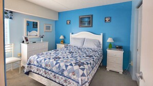 A bedroom with a bed, a dresser, a chair, and a nightstand with a lamp.