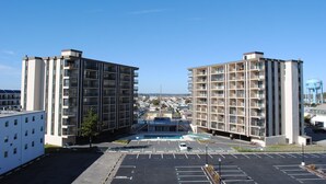A modern apartment building with multiple floors and balconies, a parking lot in front, and a clear blue sky.