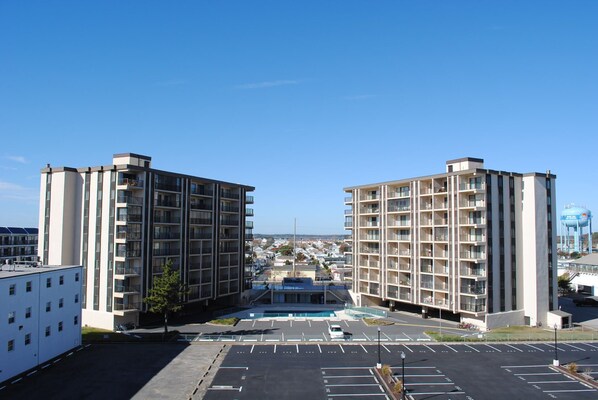 A modern apartment building with multiple floors and balconies, a parking lot in front, and a clear blue sky.