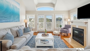 A spacious living room with a large window, a fireplace, and a ceiling fan. - Heatable Pool, Short Walk to Beach, Luxury Living! Sweet Carolina (Folly Beach)