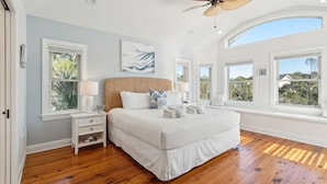 A bedroom with a large bed, wooden flooring, a ceiling fan, and multiple windows. - Heatable Pool, Short Walk to Beach, Luxury Living! Sweet Carolina (Folly Beach)