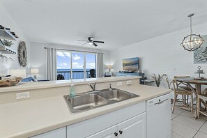 A modern kitchen with a double sink, a ceiling fan, and a view of the ocean through large windows.