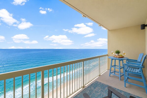 A balcony with a view of the ocean, a table with two chairs, and a small potted plant.