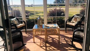 Patio soleggiato con mobili in vimini, un tavolino e vista su un campo da golf.