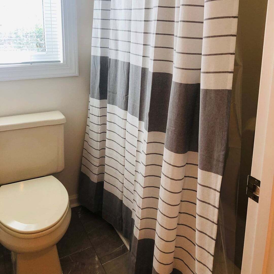 A bathroom with a toilet, a shower curtain with horizontal stripes, and a window with blinds.