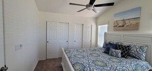A bedroom with a bed, a ceiling fan, two white doors, and a beach scene painting.
