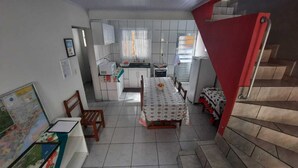Uma cozinha compacta com armários brancos, uma mesa de jantar com toalha de mesa estampada e uma escada vermelha.
