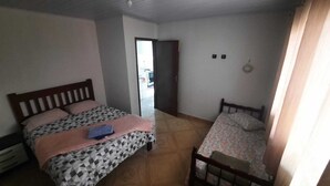 Quarto com uma cama grande, uma cama menor e uma mesa de cabeceira de madeira.