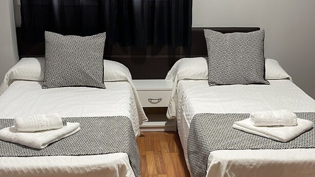 Habitación doble con dos camas, cada una con almohadas estampadas y una toalla blanca.