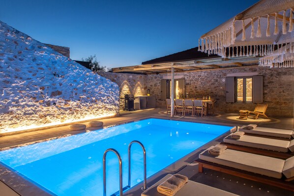 Relax by the serene pool surrounded by a stone wall and wooden deck, with a cozy seating area for dining or unwinding.