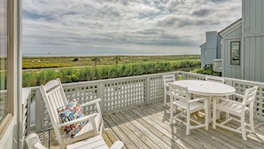 A wooden deck with white furniture, a view of the beach, and a grassy area.