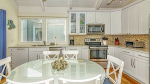 A modern kitchen with white cabinetry, a glass dining table, and a ceiling fan.