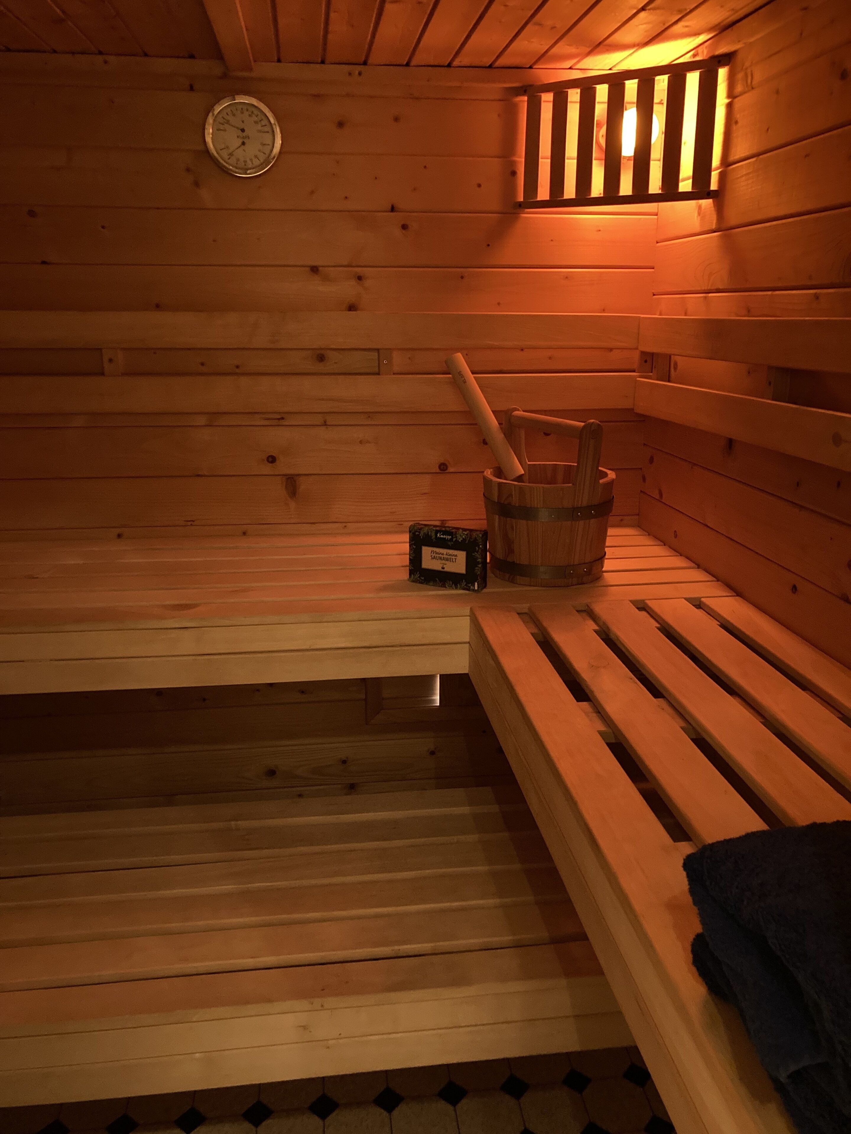 A wooden sauna with benches, a wooden bucket, and a thermometer.