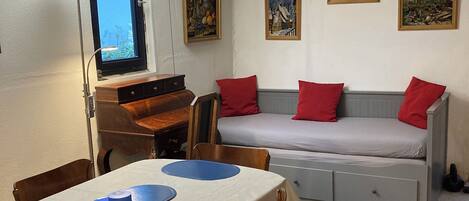 A cozy room with a dining table, chairs, a sofa, and a window.